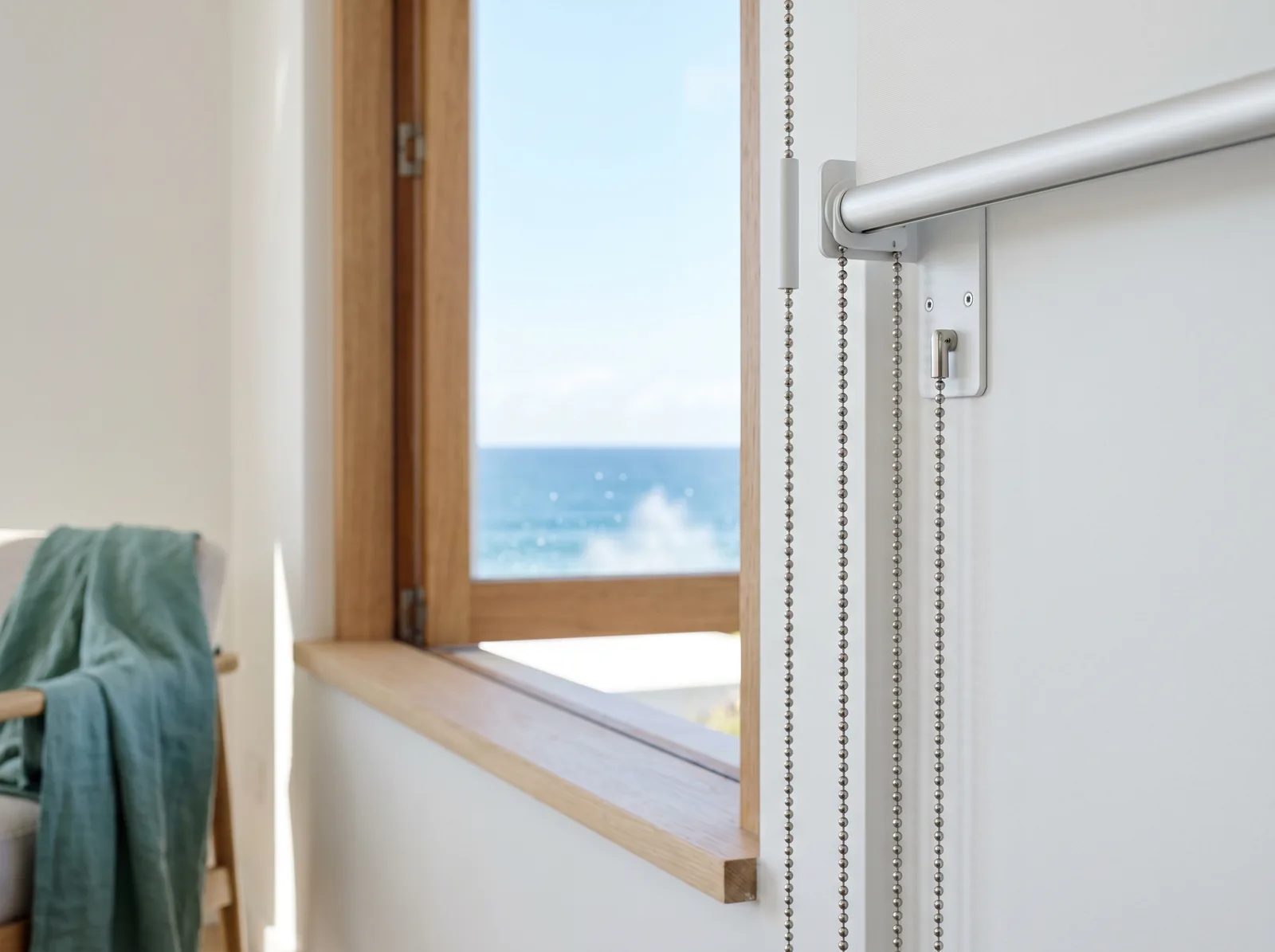 Clean stainless blind chain and bracket beside an open window with the ocean beyond