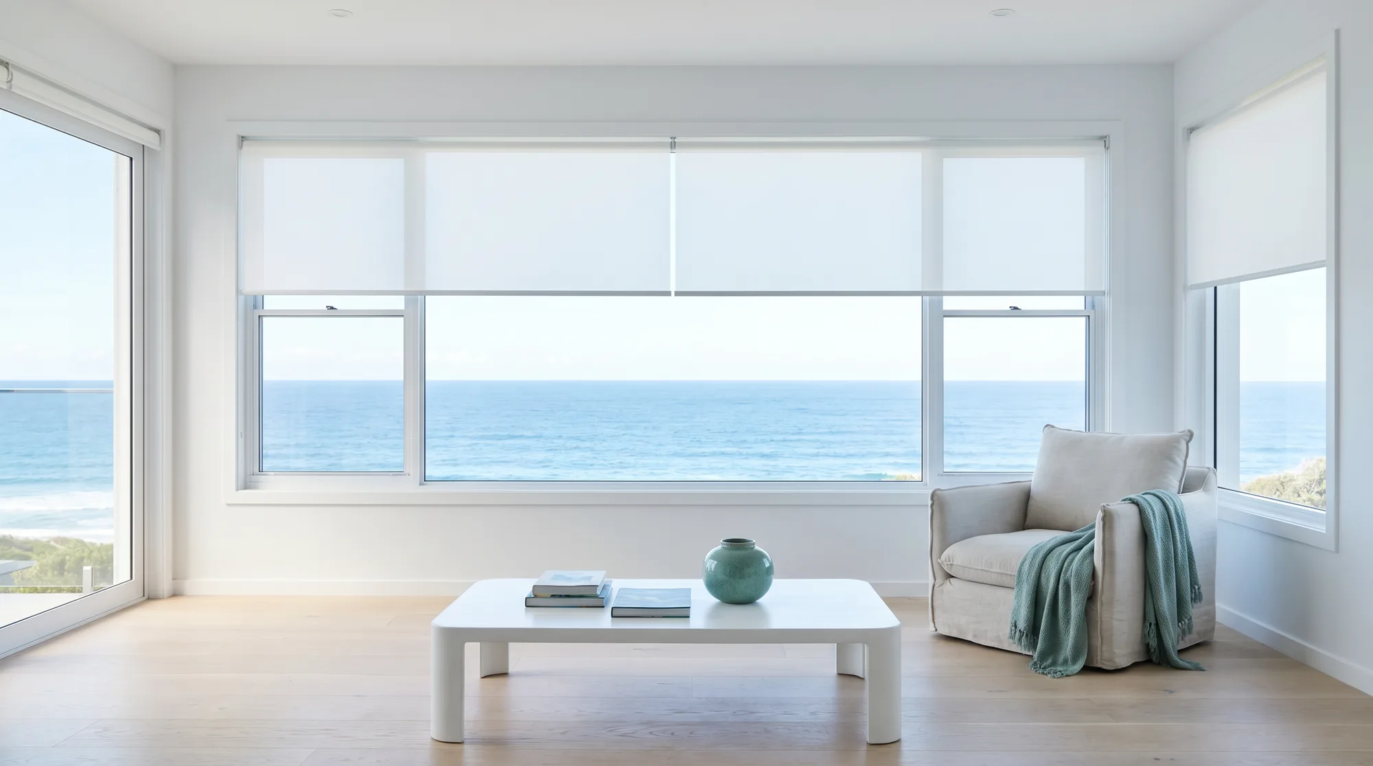 Bright coastal living room with light-filter roller blinds lowered to half, morning light spread evenly across the room