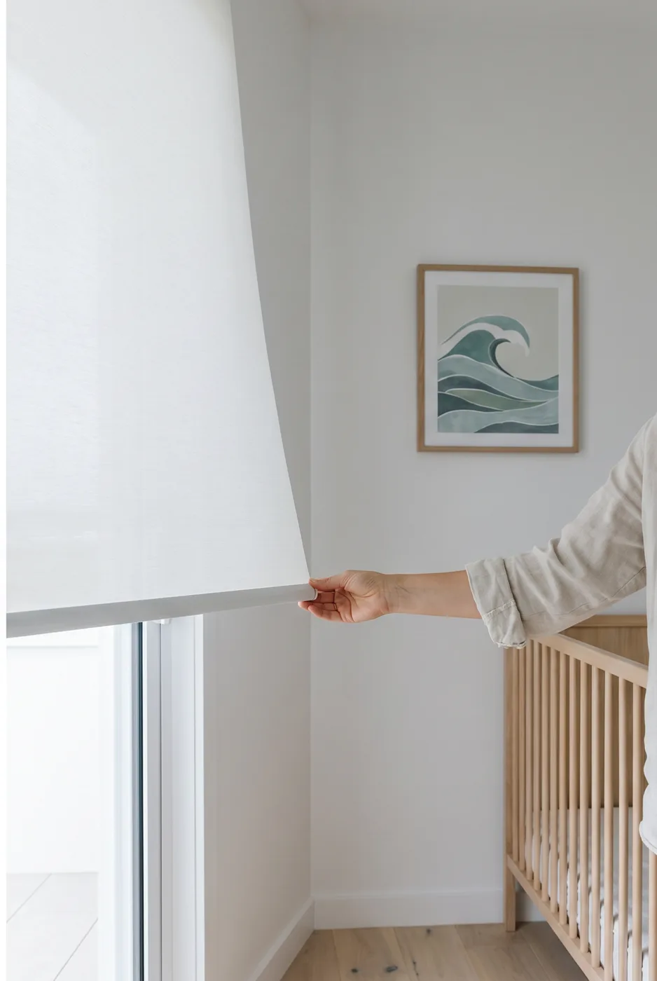 Hand drawing a cordless roller blind down by its bottom rail in a nursery, no cord or chain on the window